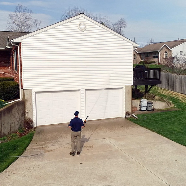 professional in blue hat and shirt washing exterior of brick and white home